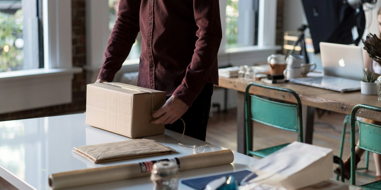 Onlinehändler verpackt an einem hellen Arbeitstisch eine Bestellung im Versandkarton, E-Commerce-Alltag hinter kostenlosen Produkteinträgen bei Google